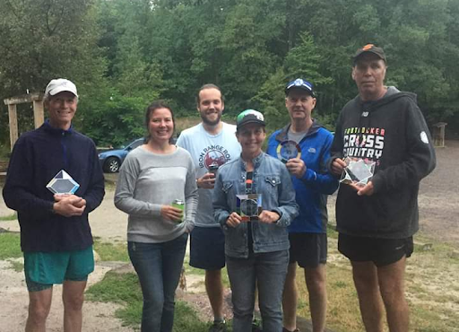 There is a group of people smiling and all holding a stained glass award. There are trees in the background.